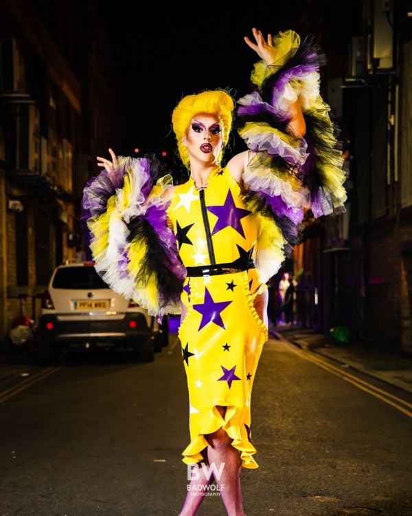 Letitia Delish in einem Latex-Outfit mit Sternenmuster und Rüschenärmeln, posierend auf einer nächtlichen Straße
